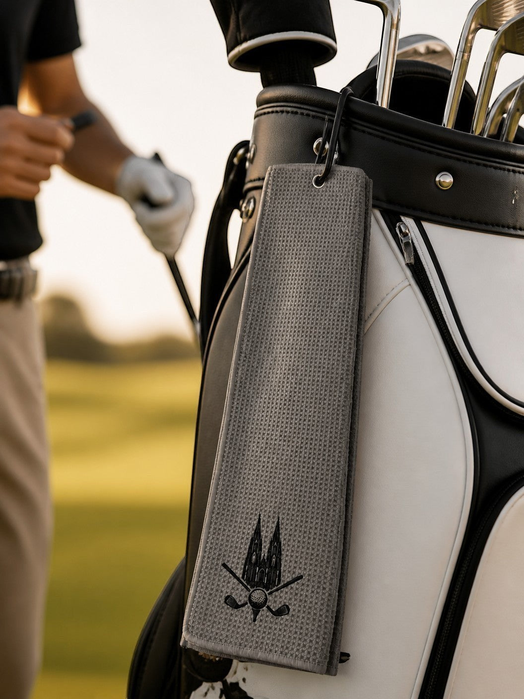 City Golf Shop Waffel-Golftuch in Grau mit Kölner Dom Motiv, befestigt an einem Golfbag auf dem Golfplatz.